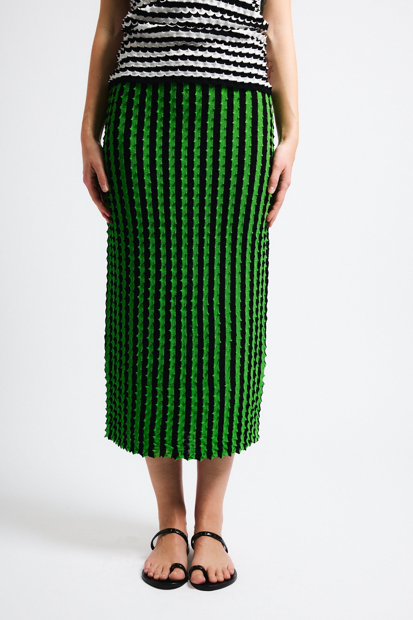 Link to "Capucine" skirt. Image is of a female model wearing black and white horizontal stripe knit crewneck shirt and vertical black/green stripe long skirt. Both pieces have a raised origami texture.