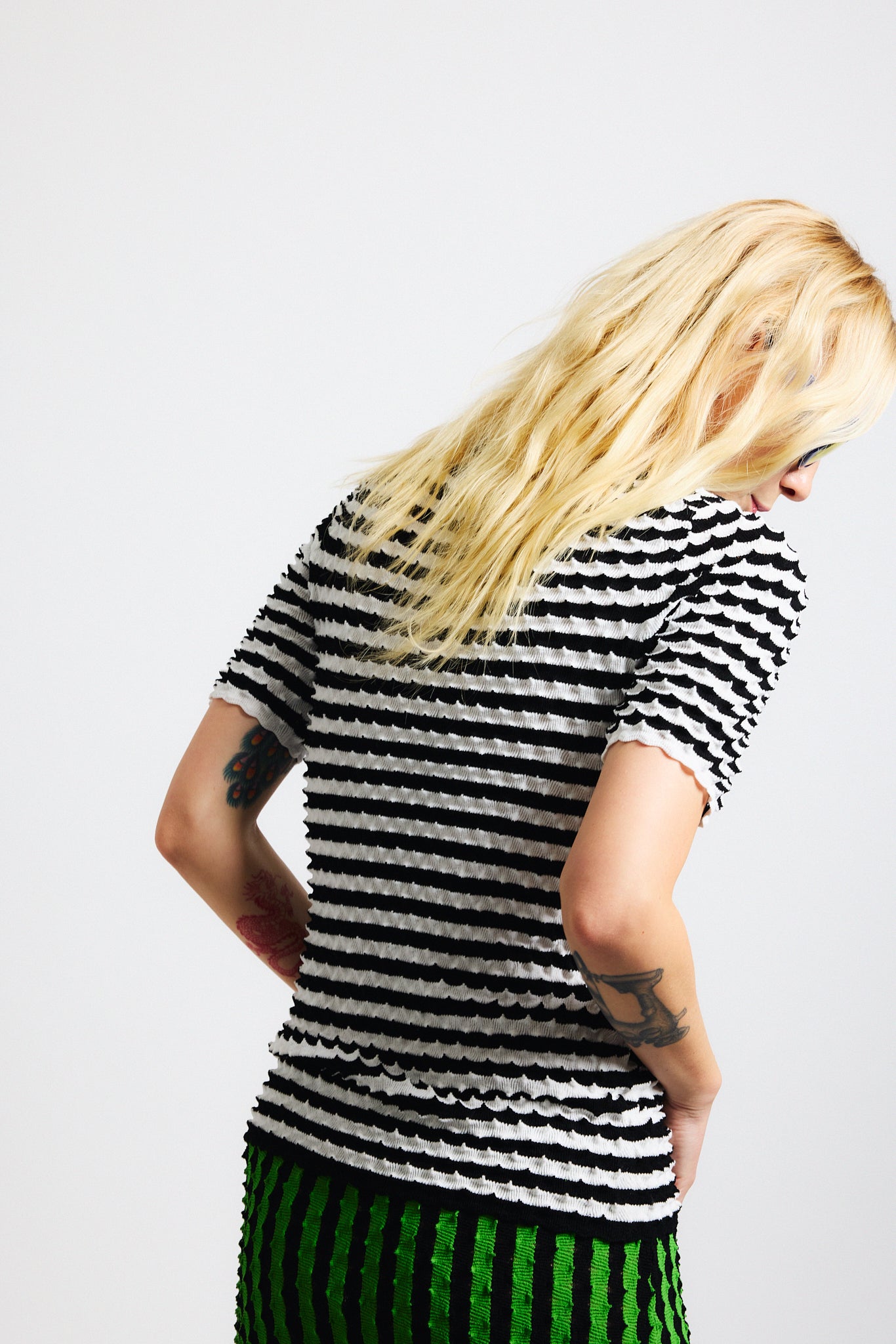 Link to "Elodie" shirt Image is of a female model wearing black and white horizontal stripe knit crewneck shirt and vertical black/green stripe long skirt. Both pieces have a raised origami texture.