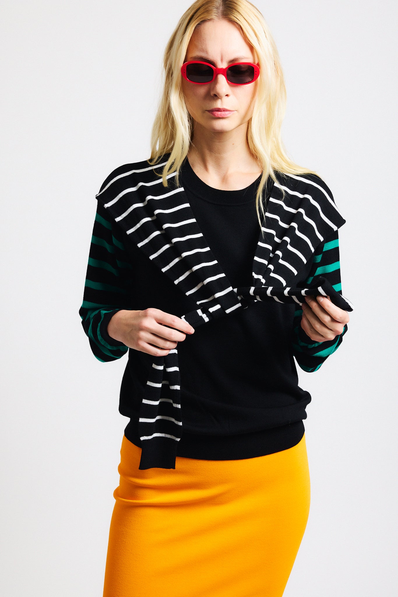 Link to "Theodore" sweater. Image is of a female model wearing black long-sleeve sweater with green striped sleeves and white striped "extra sleeve" detailing at the shoulder tied in the front.