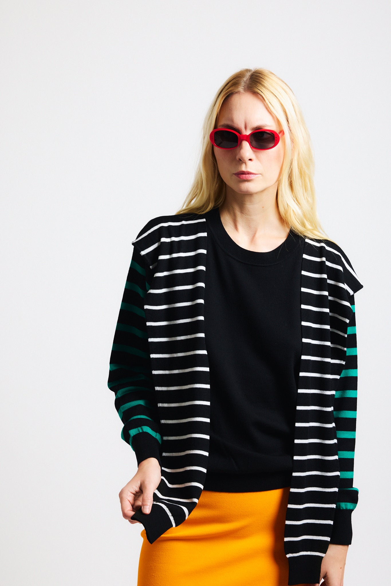 Link to "Theodore" sweater. Image is of a female model wearing black long-sleeve sweater with green striped sleeves and white striped "extra sleeve" detailing at the shoulder tied in the front.