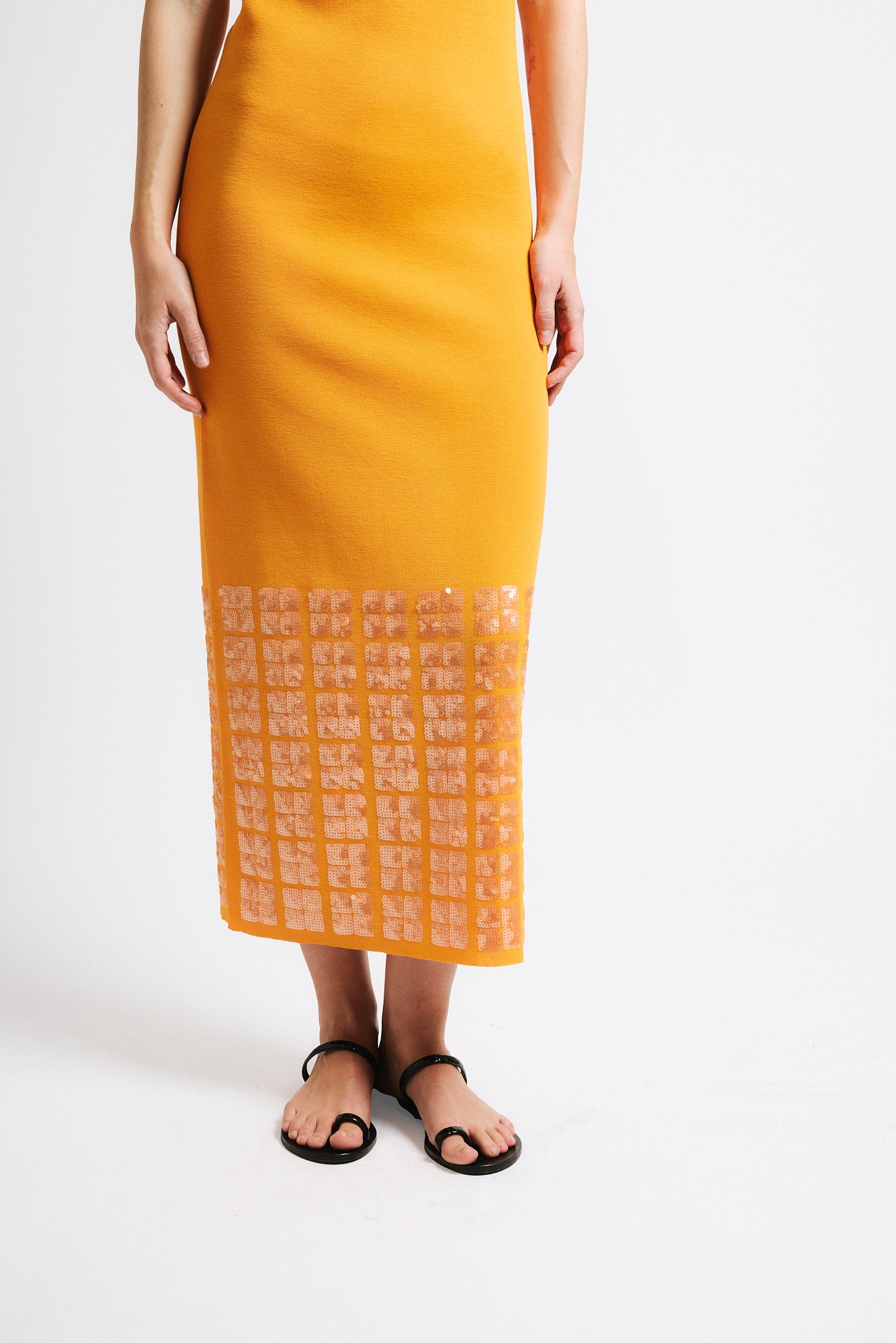 Link to "Tosca" dress. Image is of a female model wearing backless crewneck bright orange dress with layered sequin hem.