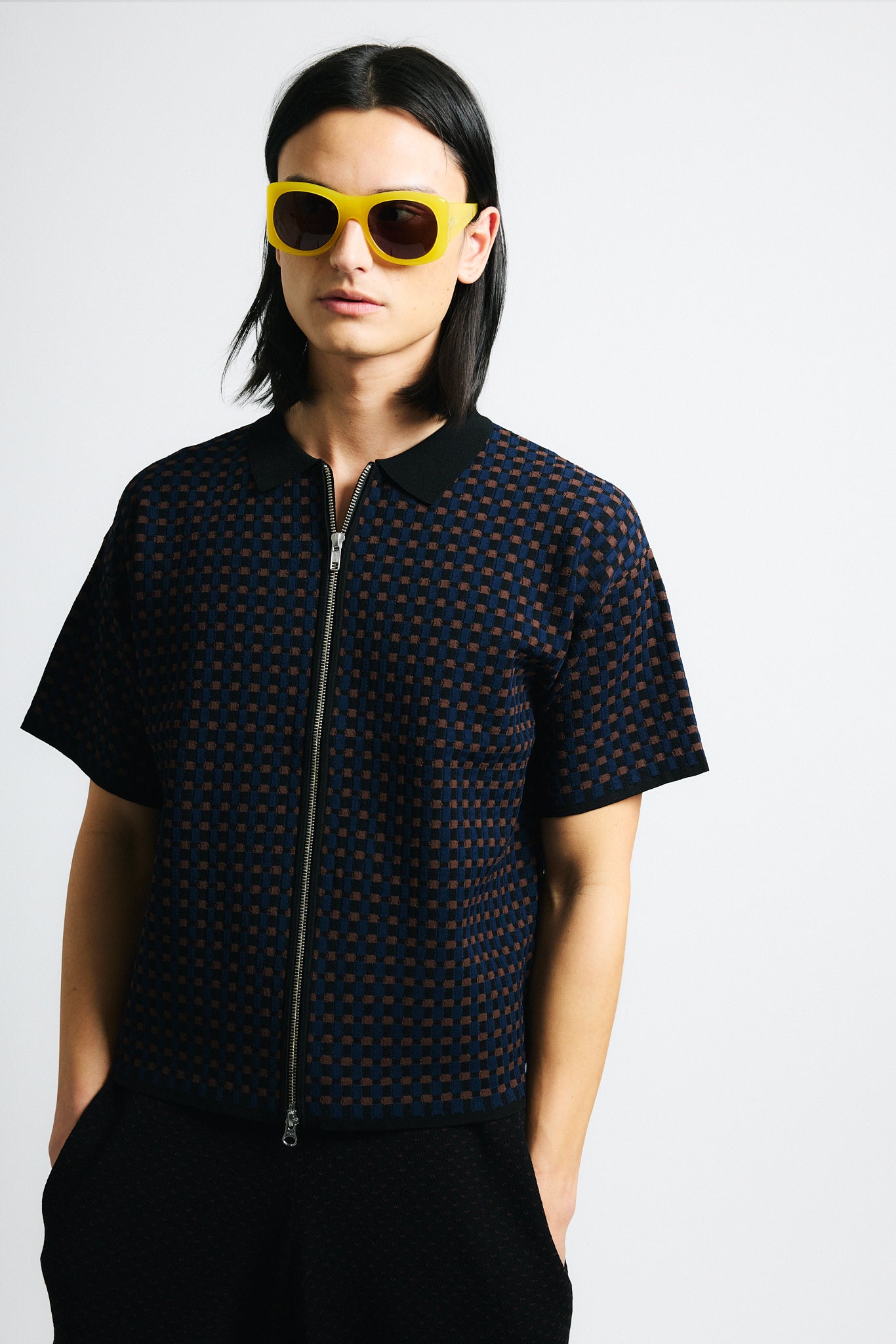 Link to "Lorenzo" polo. Image is of a male model wearing brown/blue/black cross hatch textured double zip polo and black shorts with yellow sunglasses. 