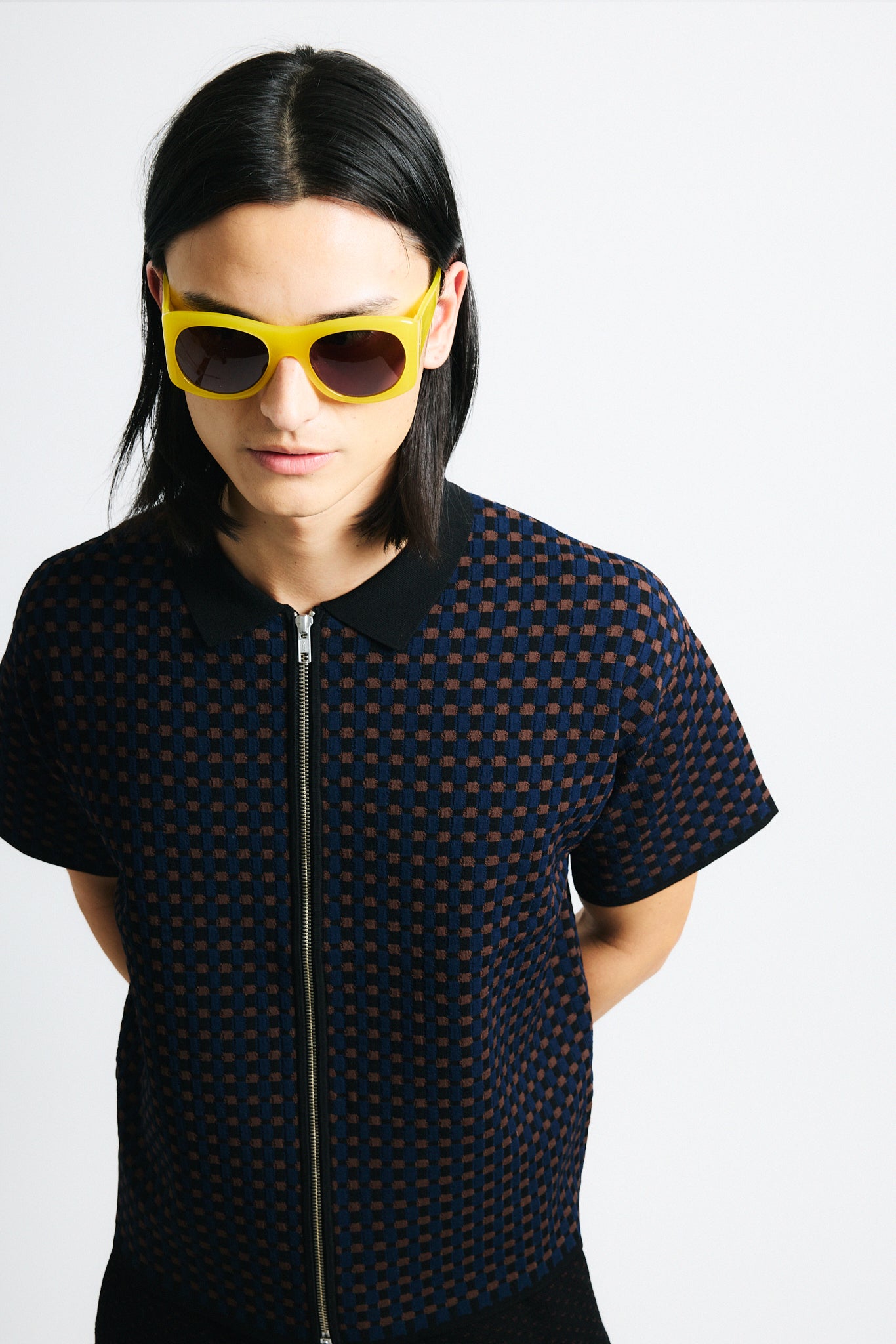 Link to "Lorenzo" polo. Image is of a male model wearing brown/blue/black cross hatch textured double zip polo and black shorts with yellow sunglasses. 