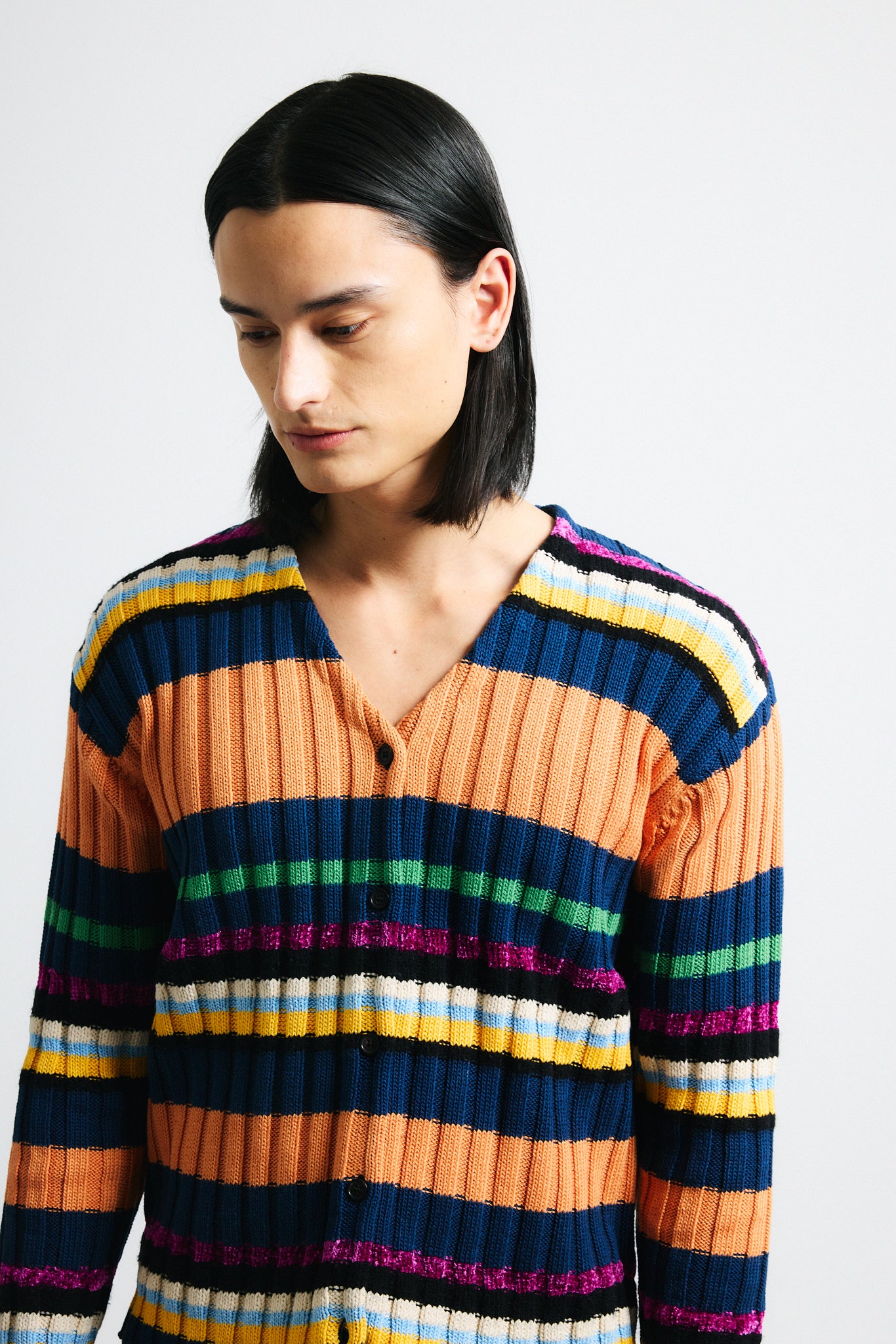 Link to "Suri" cardigan. Image is of a male model wearing orange, navy blue, and pink multi-candy striped wide ribbed cardigan with black shorts.