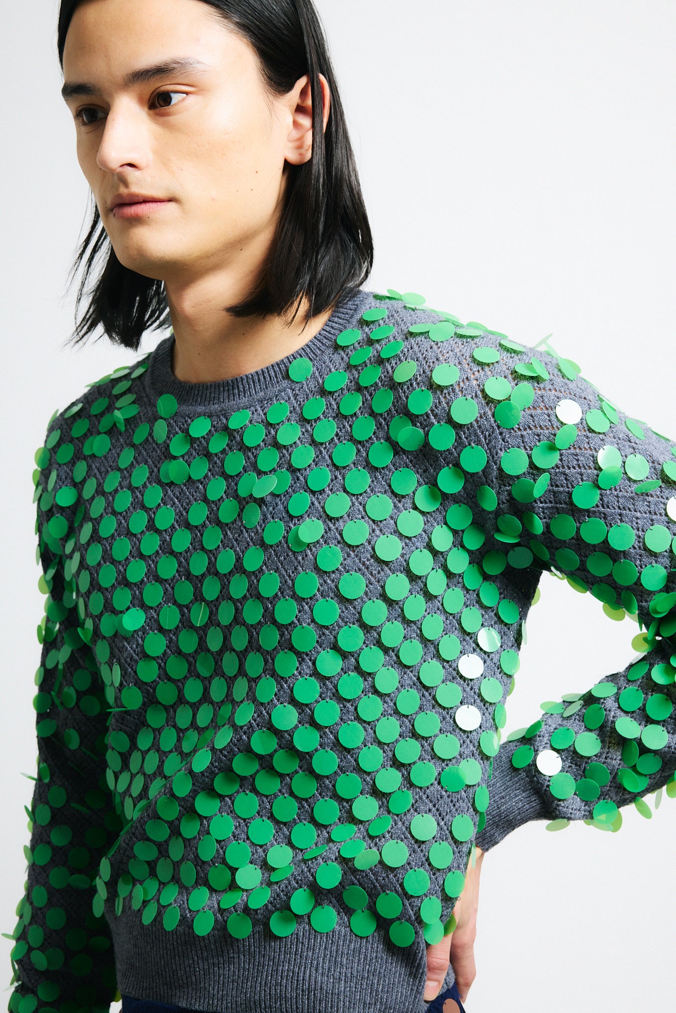 Link to "Ilaria" sweater. Image is of a male model wearing grey texture cropped crewneck sweater with green paillettes and matching pencil skirt. 