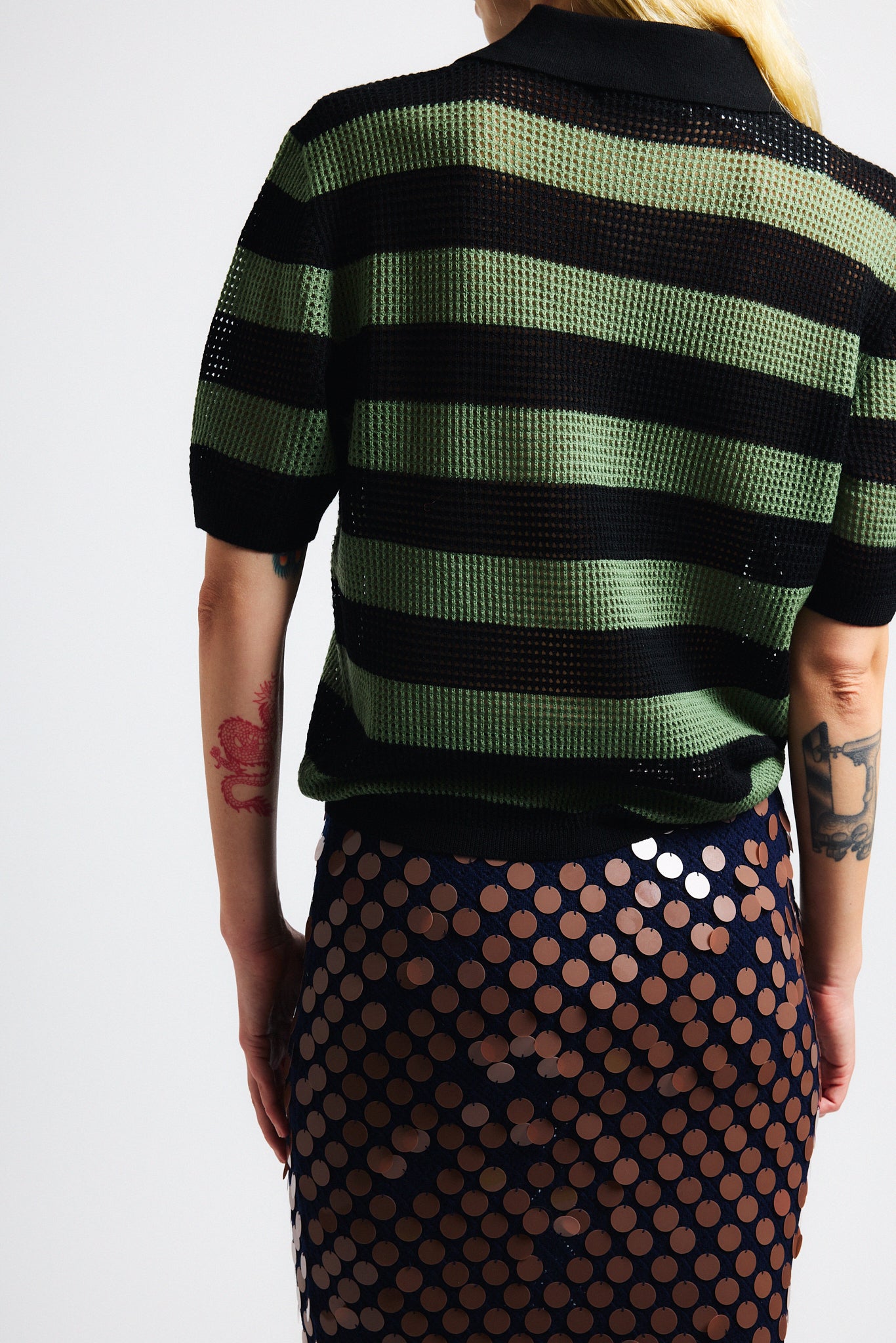 Link to "Matteo" skirt. Image is of a female model wearing green and black perforated stripe polo shirt and navy black/brown sequin knit skirt.