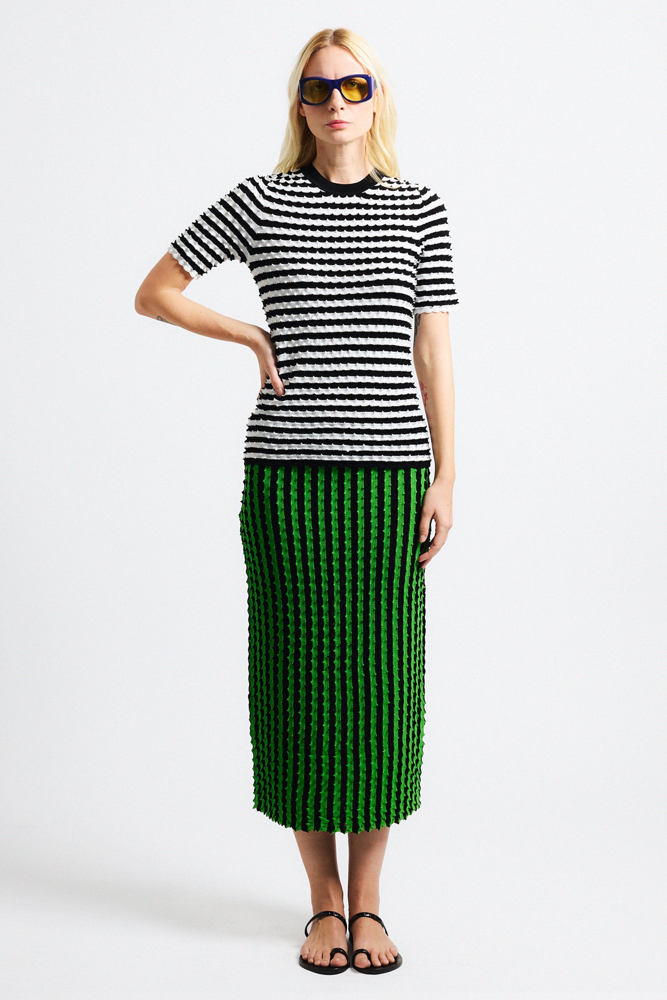 Link to "Elodie" shirt Image is of a female model wearing black and white horizontal stripe knit crewneck shirt and vertical black/green stripe long skirt. Both pieces have a raised origami texture.