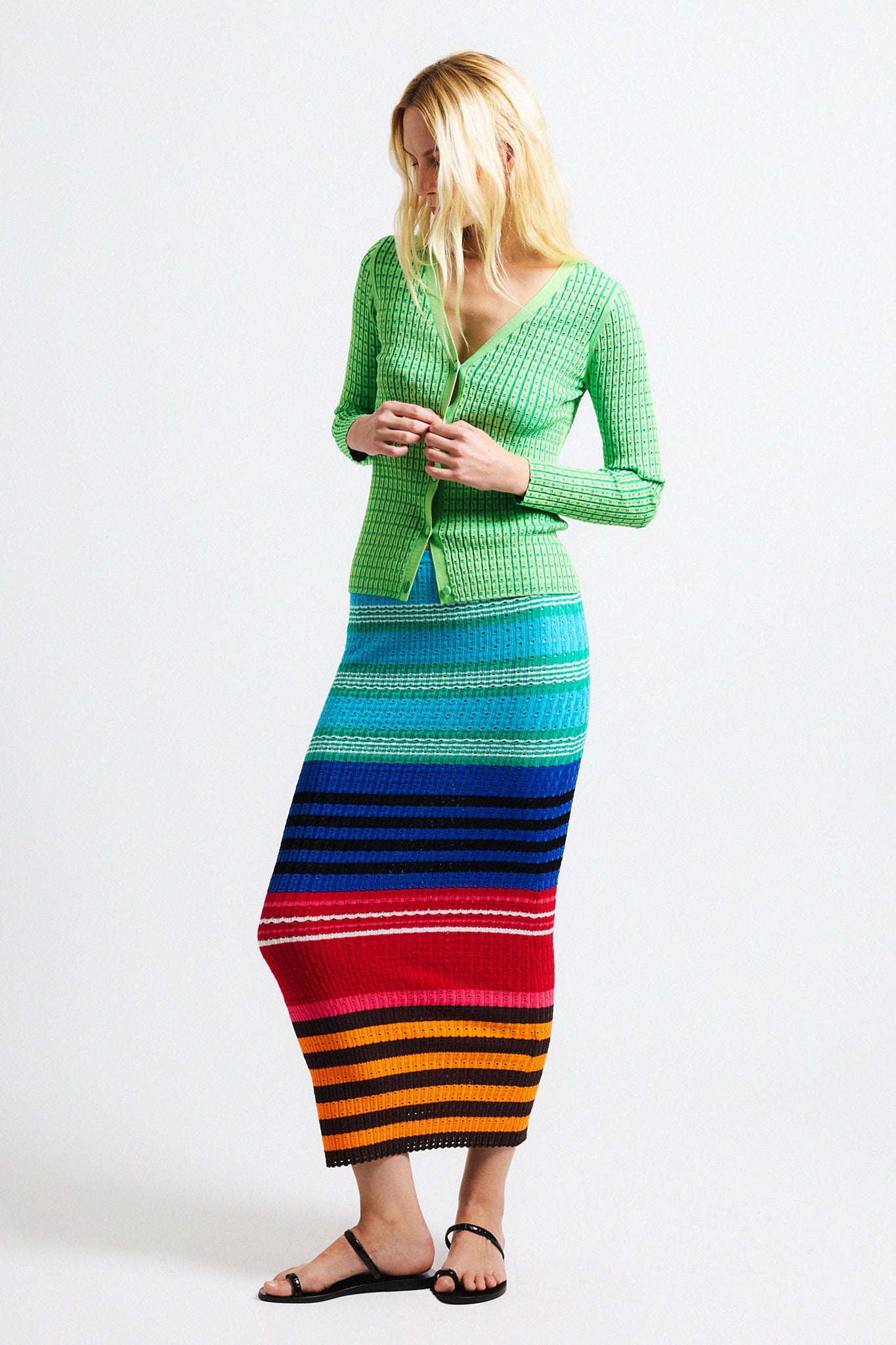 Link to "Edith" fitted skirt. Image is of a female model wearing green vertical ribbed fitted V-neck cardigan with pointelle texture and matching textured bright multi-colored long fitted knit skirt. 