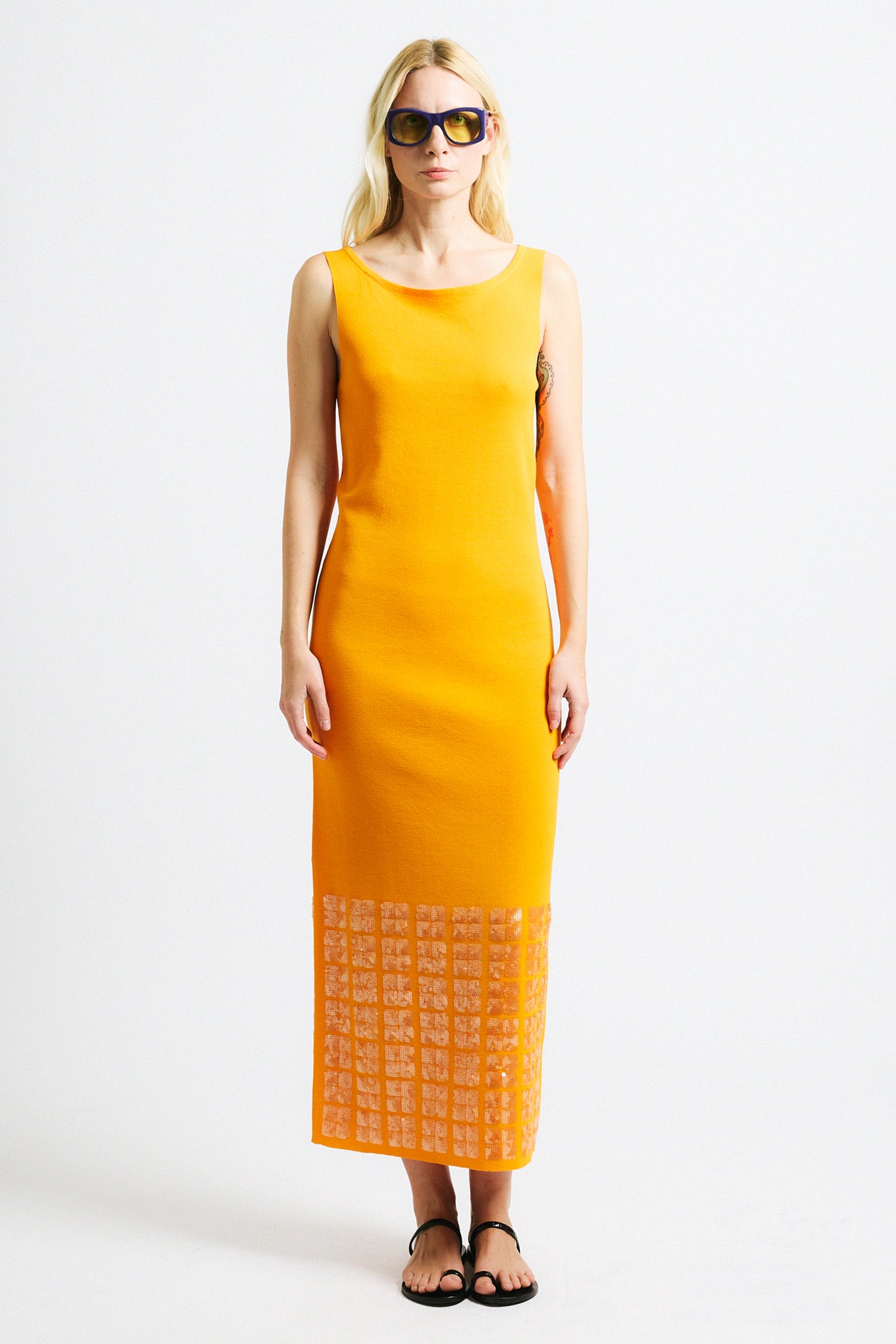 Link to "Tosca" dress. Image is of a female model wearing backless crewneck bright orange dress with layered sequin hem.