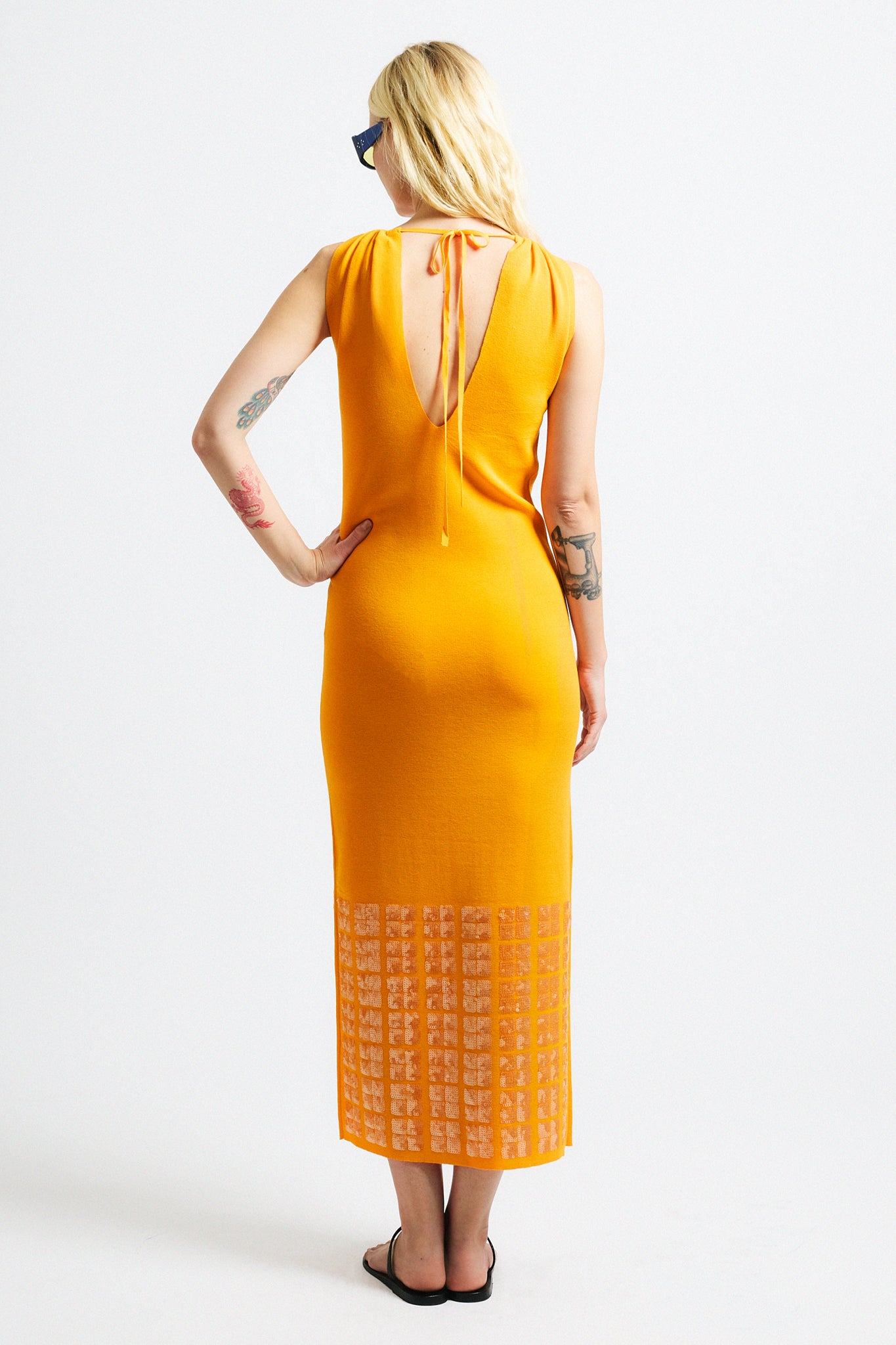 Link to "Tosca" dress. Image is of a female model wearing backless crewneck bright orange dress with layered sequin hem.