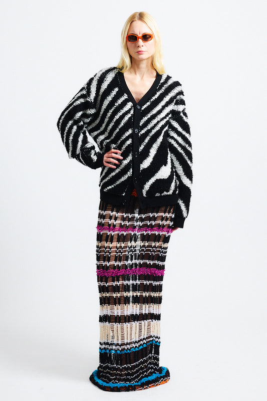 Link to "Christian" cardigan. Image is of a female model wearing "oil spill"/"zebra" print fuzzy v-neck cardigan in black and white stripes with black see-through striped knit dress and orange sunglasses. 