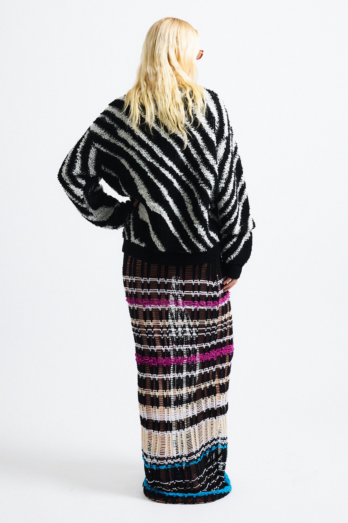 Link to "Christian" cardigan. Image is of a female model wearing "oil spill"/"zebra" print fuzzy v-neck cardigan in black and white stripes with black see-through striped knit dress and orange sunglasses. 