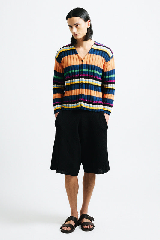 Link to "Suri" cardigan. Image is of a male model wearing orange, navy blue, and pink multi-candy striped wide ribbed cardigan with black shorts.