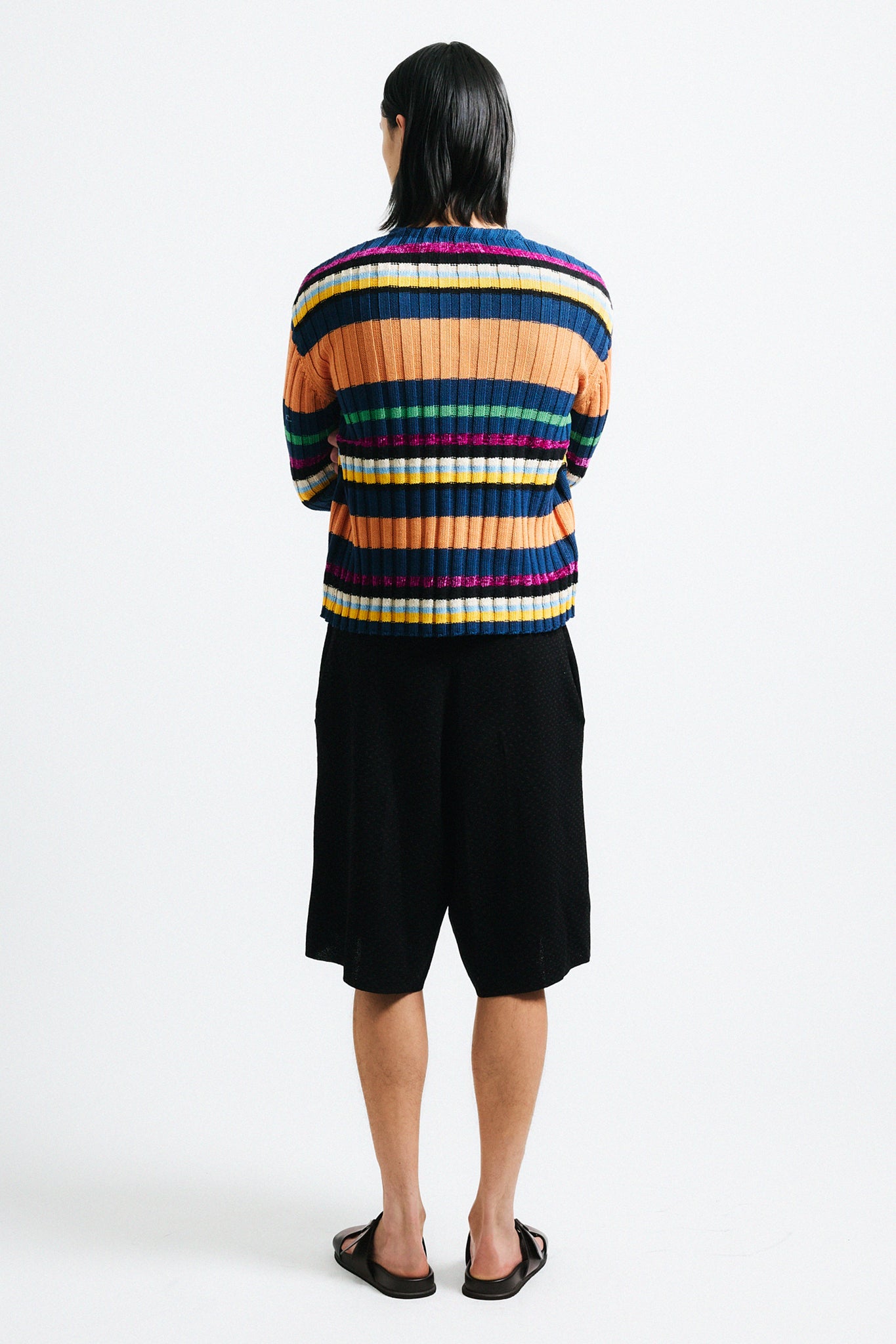 Link to "Suri" cardigan. Image is of a male model wearing orange, navy blue, and pink multi-candy striped wide ribbed cardigan with black shorts.