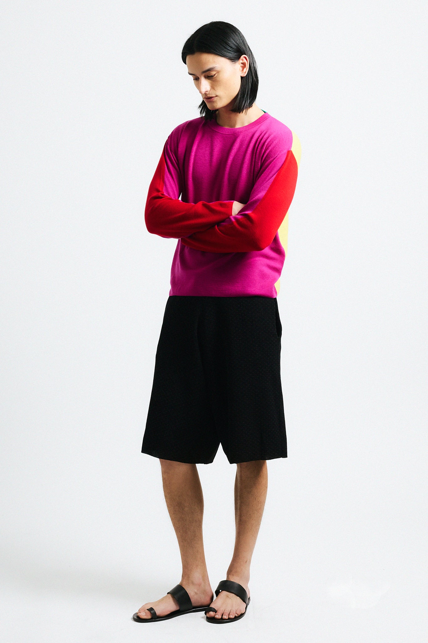 Link to "Julienne" sweater. Image is of a male model wearing magenta, red and yellow color-block sweater and black shorts. Front is pink with red sleeves and yellow back. 