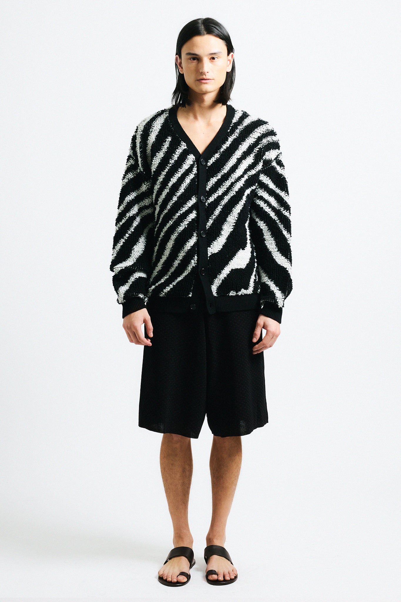 Link to "Christian" cardigan. Image is of a male model wearing "oil spill"/"zebra" print fuzzy v-neck cardigan in black and white stripes with black shorts.